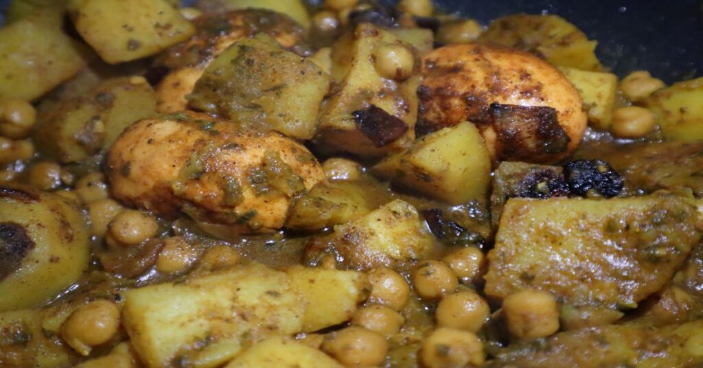 close up of egg curry recipe with hard boiled eggs, potatoes, and garbanzo beans in a pan