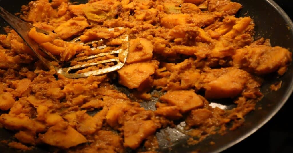 Curry pumpkin in a pan being smashed with a spatula with holes