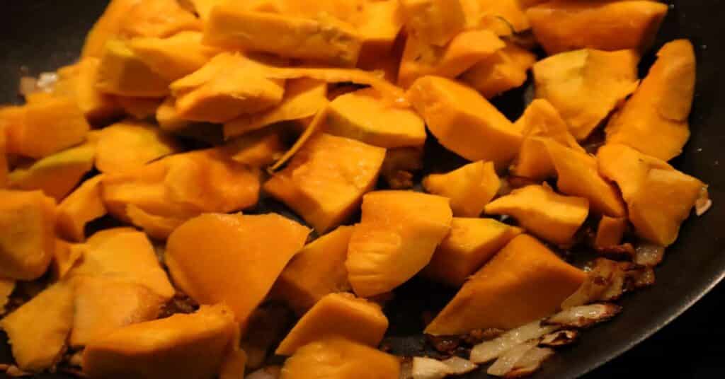 Close up of diced pumpkin over onions, garlic, and olive oil in a non-stick sauté pan