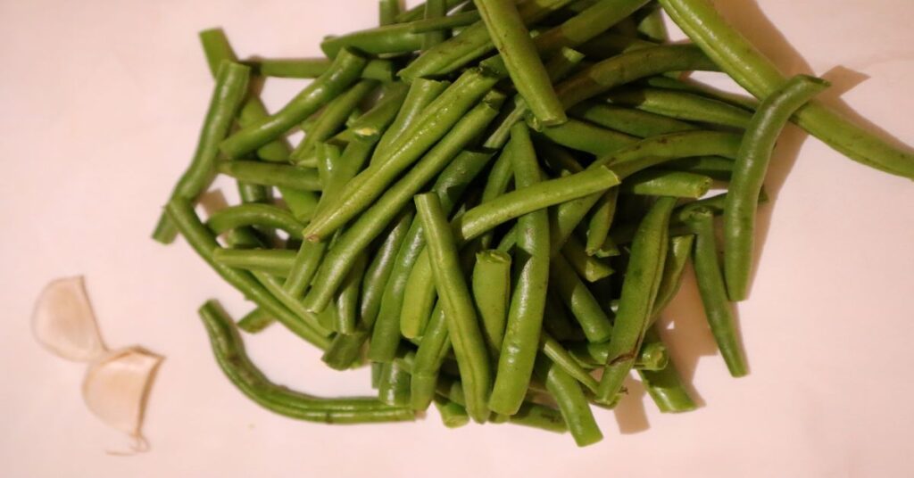 Fresh green beans and 2 cloves of garlic on a white background