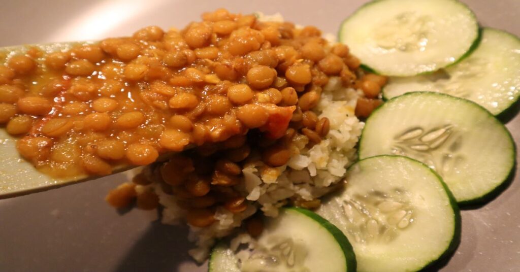 lentil recipe served with cauliflower rice and sliced cucumbers on a gray plate 