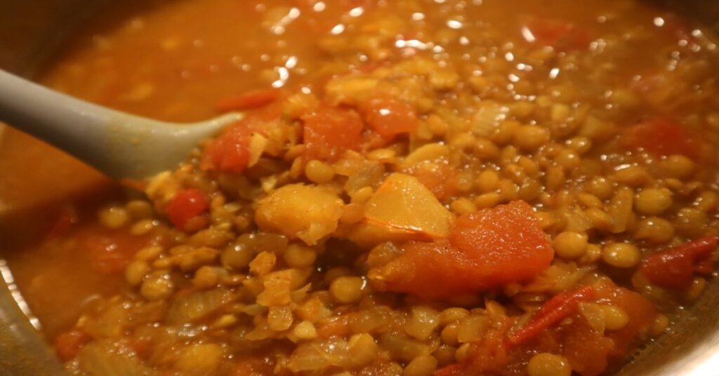 Lentil recipe and lentil soup recipe finished. You can see the tomatoes, pumpkin, and tomatoes on the gray spoon in the pot. 