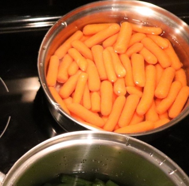 Black stovetop with baby carrots submerged in water