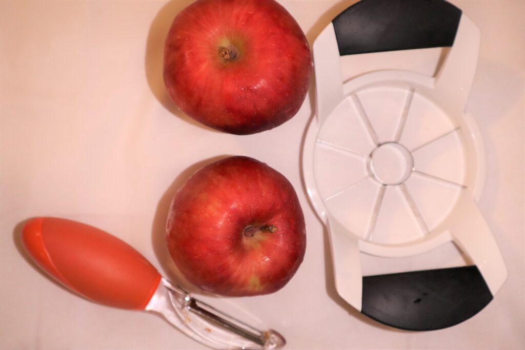 Two red apples, one apple corer, and a vegetable peeler on a white background