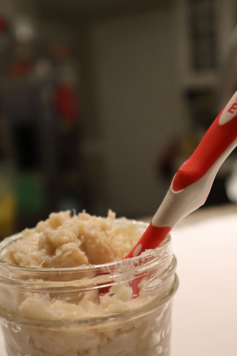 Apple chicken pureed baby food in a small mason jar with a red infant spoon sticking in it on a counter top with steel fridge in background