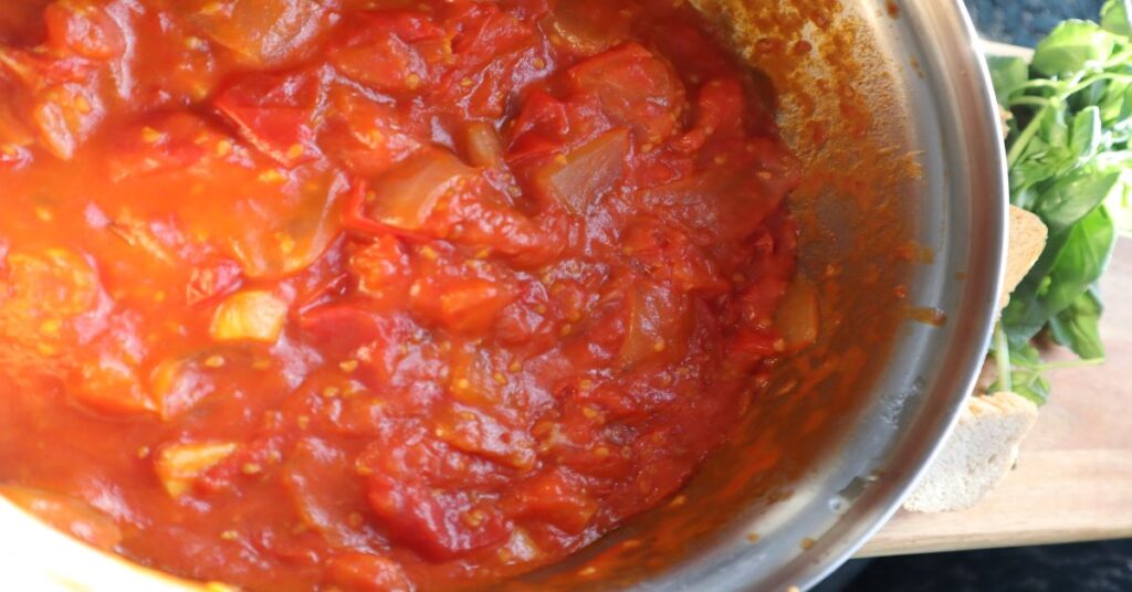 Homemade Tomato Sauce for Pasta in pot next to fresh basil and croutons on a wooden board