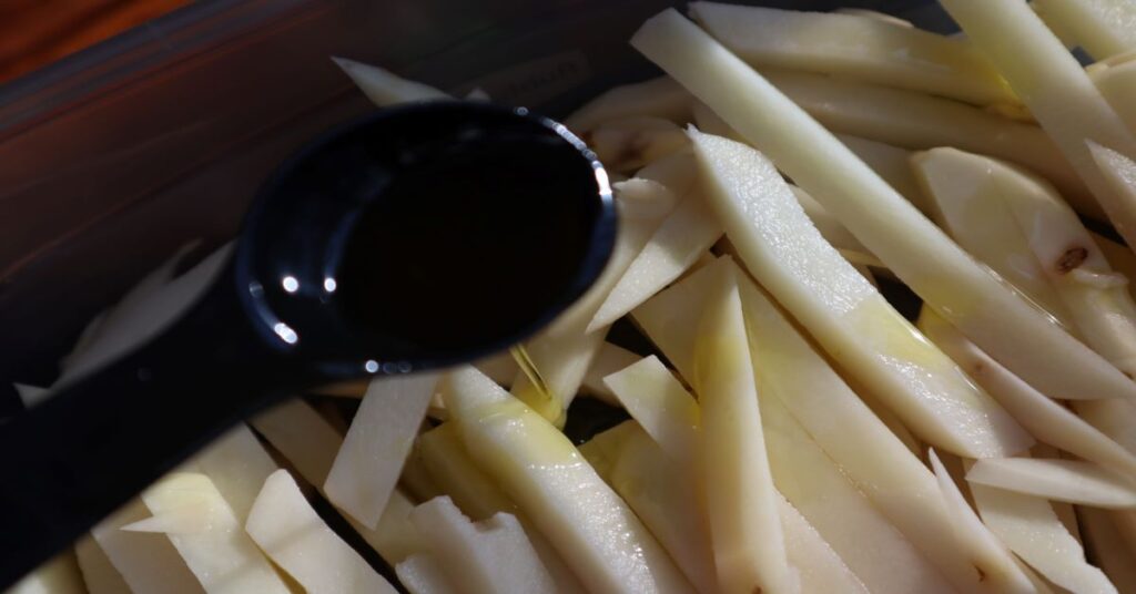 raw potatoes sliced and peeled ready for air fryer with olive oil being poured on