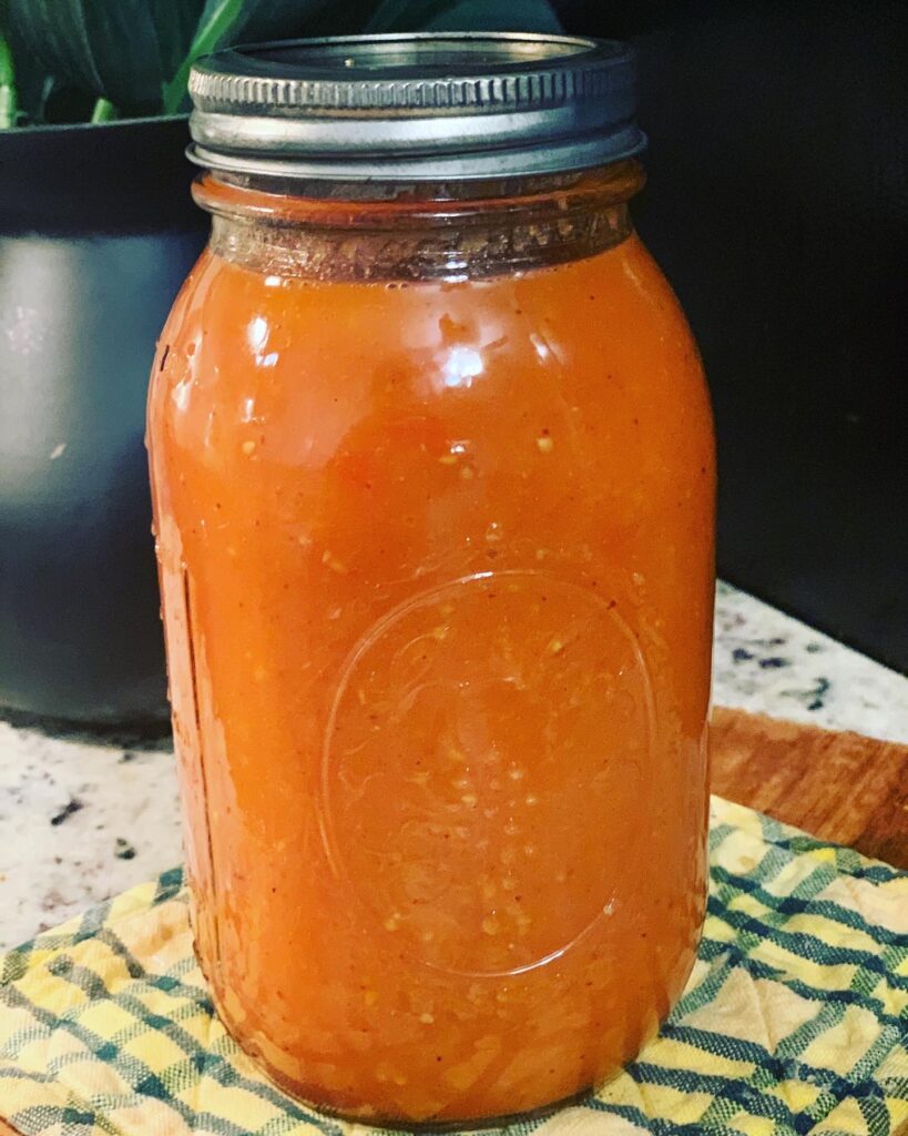 homemade tomato soup in mason jar on a cherry wood background with a spoon and green and yellow and yellow and white checkered handcloths in background