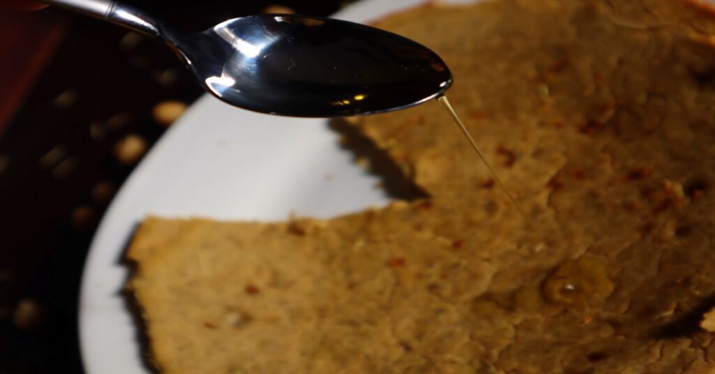 Farinate on a white plate with one slice missing. A spoon with olive oil on top being drizzled