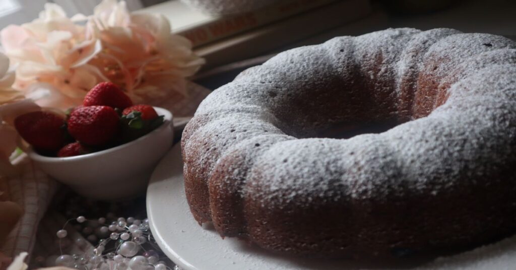 Strawberry champagne pound cake on white plate and strawberries in small cup and flowers in background