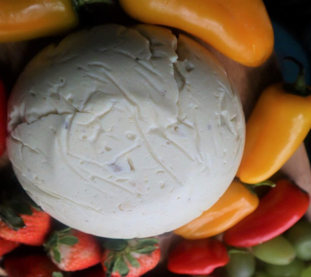 Vegan Cheese Recipe displayed on a fruit and veggie board. One the board here are strawberries and yellow and red mini bell peppers, also green grapes