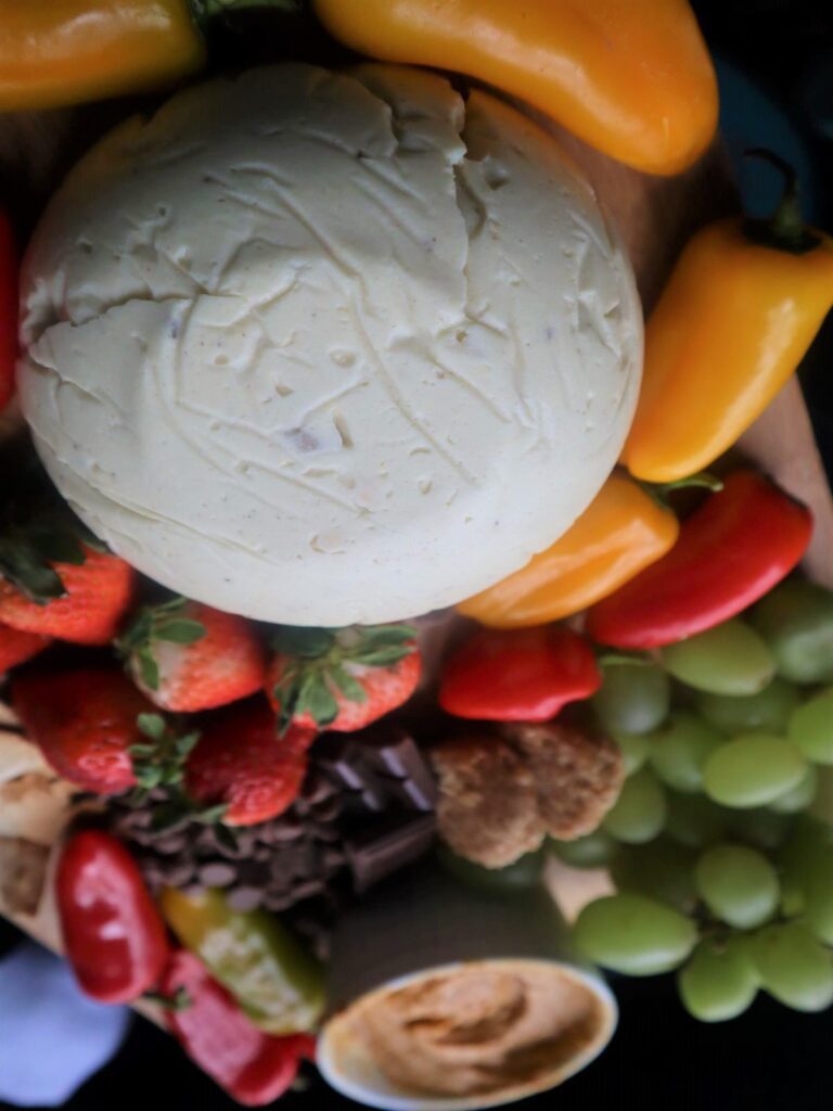 Vegan Cheese Recipe displayed on a fruit and veggie board (strawberries, green grapes, mini bell peppers in red and yellow, and chocolate)