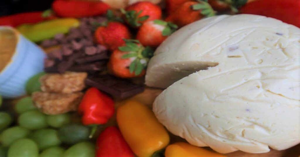 Vegan Cheese Recipe displayed on a fruit and veggie board (strawberries, green grapes, mini bell peppers in red and yellow, and chocolate)