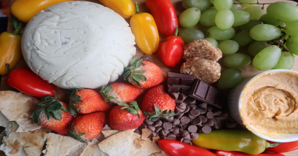 Vegan Cheese Recipe displayed on a fruit and veggie board (strawberries, green grapes, mini bell peppers in red and yellow, and chocolate)