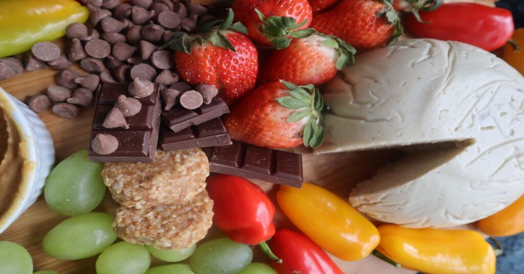 Vegan Cheese Recipe displayed on a fruit and veggie board (strawberries, green grapes, mini bell peppers in red and yellow, and chocolate)