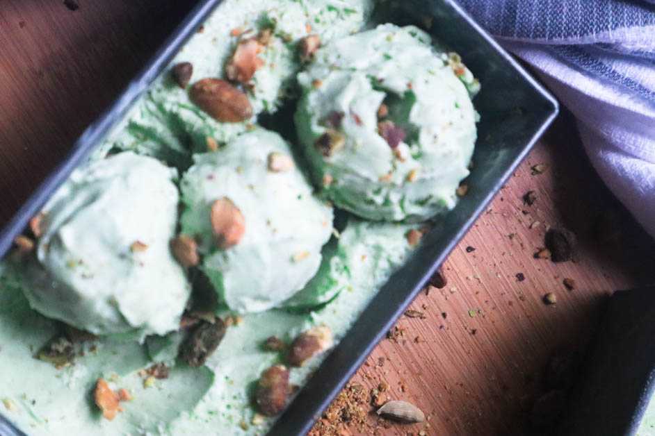 Pistachio Cardamom Ice Cream in gray rectangular container with pistachio pieces on top and ice cream is in three scoops
