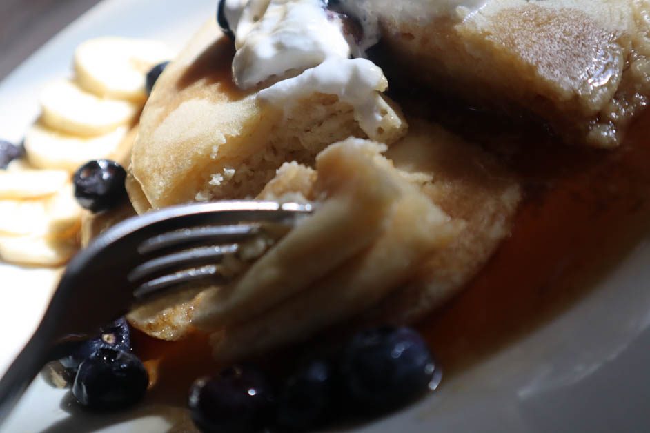 Short stack of pancakes topped with whipped cream and blueberries in a pool of maple syrup