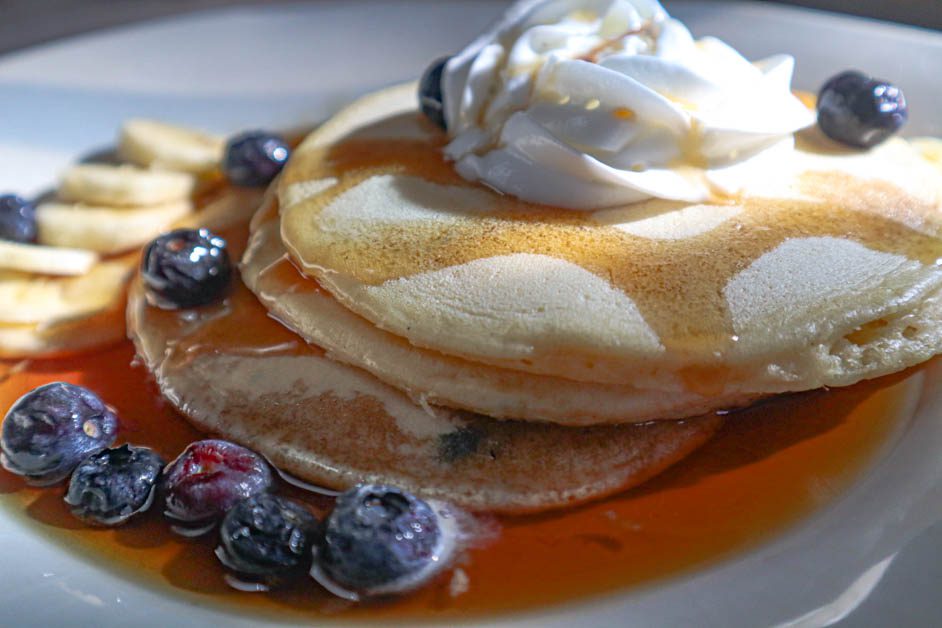 Short stack of pancakes topped with whipped cream and blueberries in a pool of maple syrup