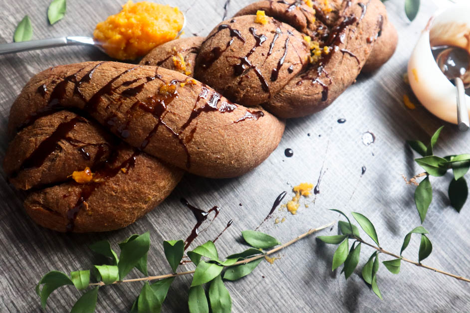 Chocolate Orange Braided Bread drizzled with chocolate syrup on a gray textured background with a silver spoon filled with orange marmalade on it.