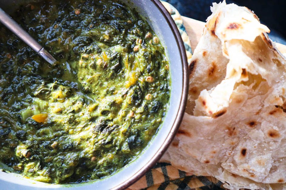 Callaloo in gray bowl next to some roti