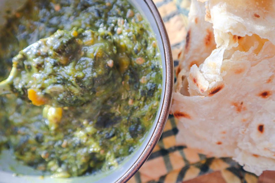 Callaloo in gray bowl next to some roti . Yellow and green checkered pan handle cover in background