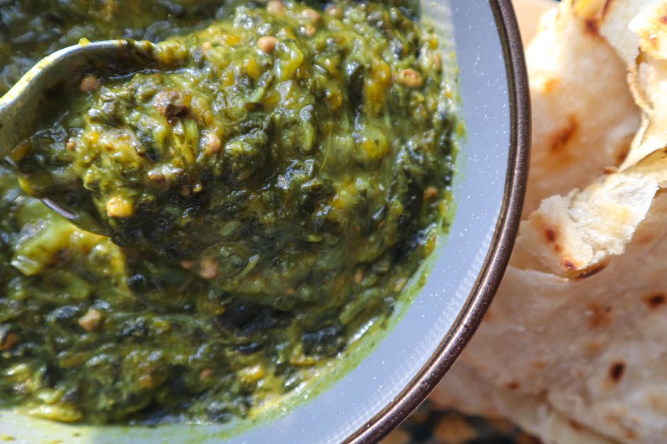 Callaloo in gray bowl next to some roti . Yellow and green checkered pan handle cover in background