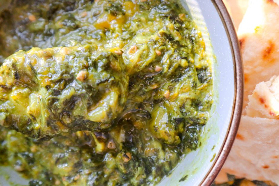 Callaloo in gray bowl next to some roti . Yellow and green checkered pan handle cover in background