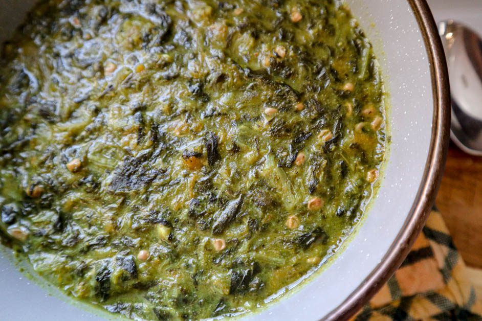 Callaloo in gray bowl. Yellow and green checkered pan handle cover in background