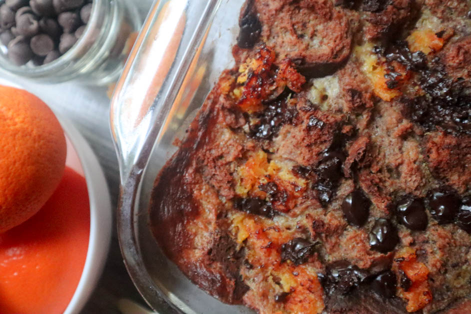 Chocolate Orange Bread Pudding in casserole dish with oranges in a white down next to chocolate chips