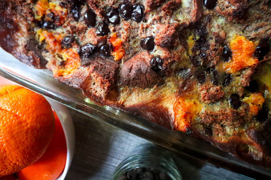 Chocolate Orange Bread Pudding in casserole dish with oranges in a white down next to chocolate chips