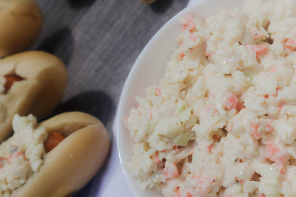 creamy coleslaw in a white bowl. Hot dog in background