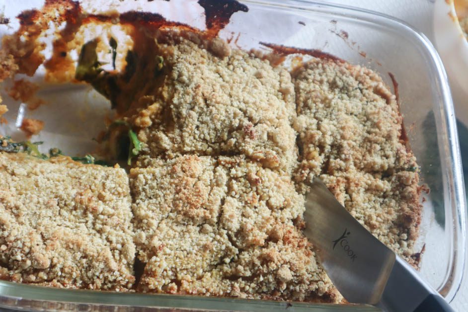 Vegan Spinach Pumpkin Lasagna with all layers displayed. Background is full tray of lasagna with one piece removed. Knife cutting a second slice